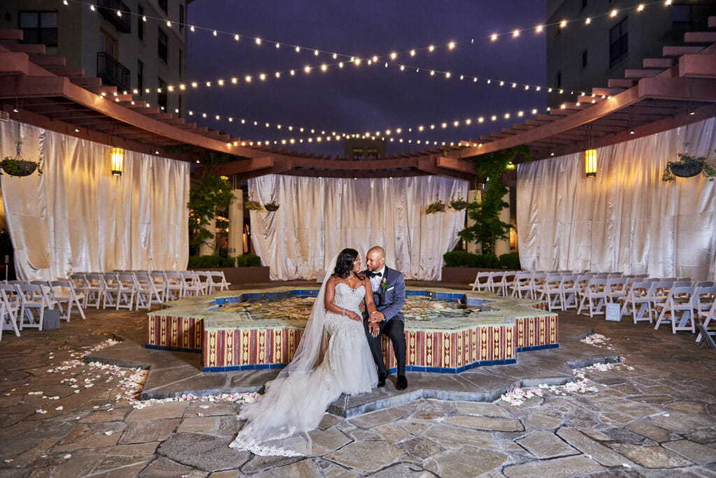wedding couple sitting on the noor terrace fountain with draping and string lights in the background