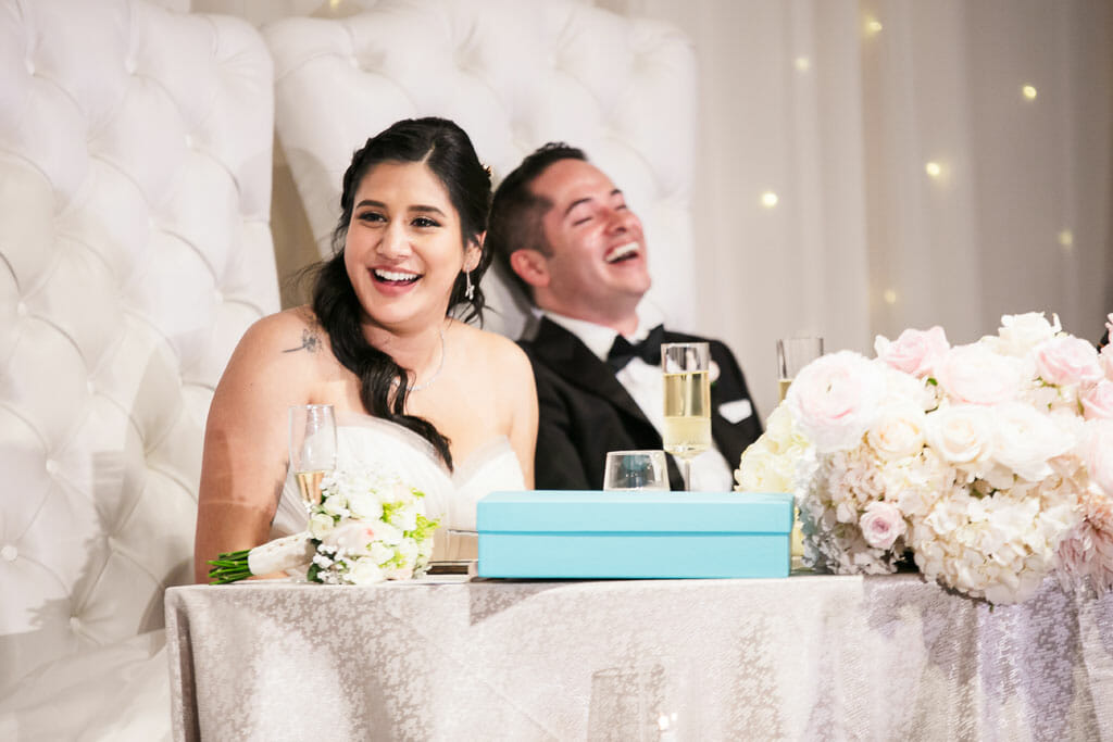 bride and groom sitting at sweetheart table laughing at speeches
