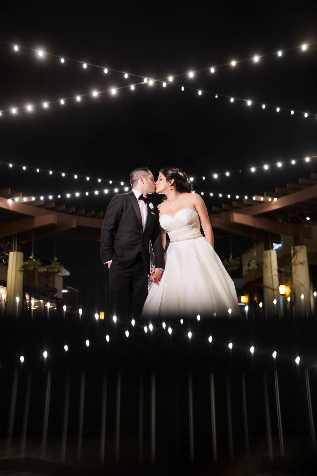 bride and groom kissing under string lights on the terrace at noor