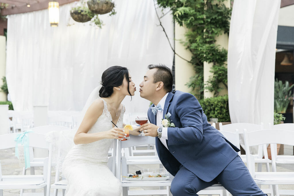couple kissing and holding cocktails after outdoor wedding ceremony