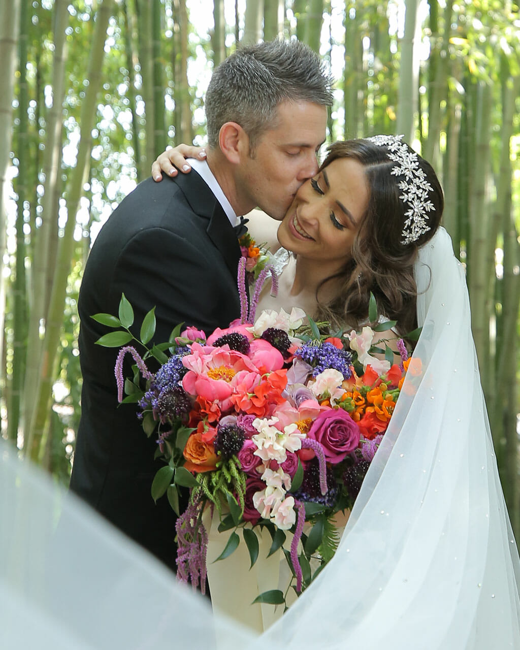 beautiful bride and groom kissing in the los angeles armboretum and holding bouquet of orange white and pink flowers
