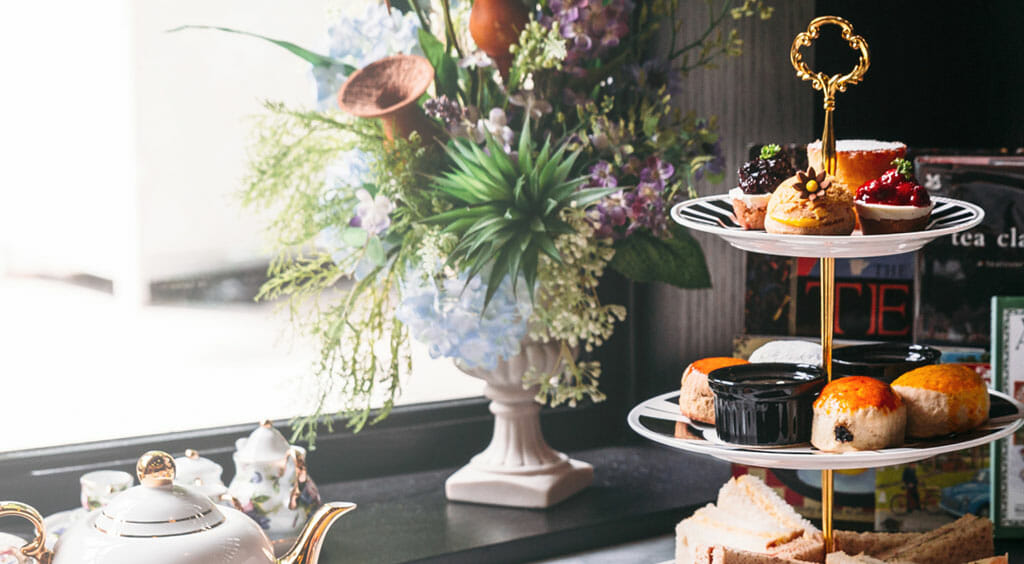 high tea for baby shower with cakes on a stand plus teapots cups and a flower arrangement