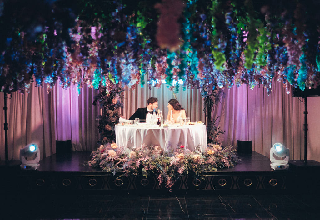 NOOR wedding banquet hall wedding couple sat at sweetheart table in the sofia banquet hall with flowers suspended from the ceiling