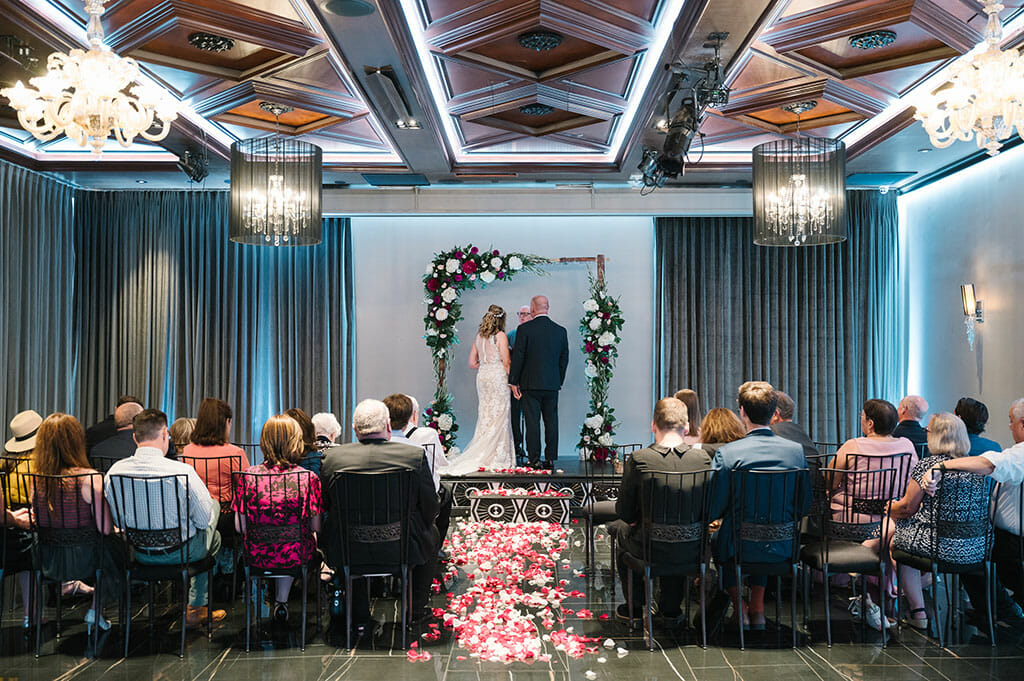 NOOR wedding venue in los angeles wedding ceremony setuip in the ella ballroom with ghost chandeliers and floral wedding arch