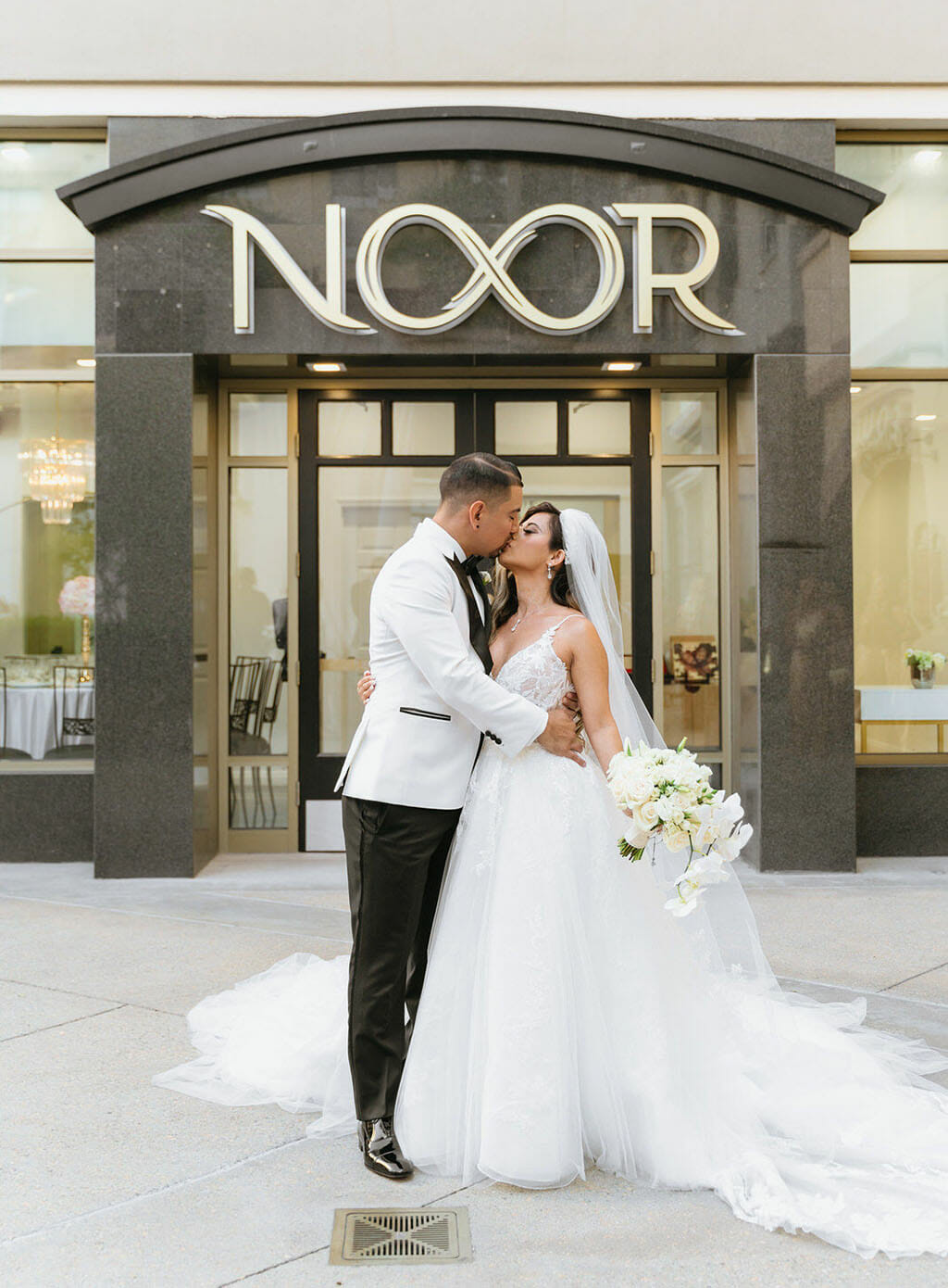 NOOR wedding couple kissing in front of pasadena banquet hall and event spaces with NOOR sign behind them