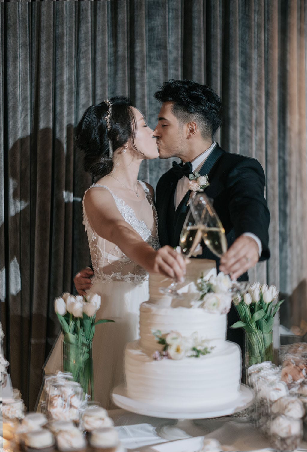 wedding couple kissing and toasting next to wedding cake in the ella ballroom at noor pasadena