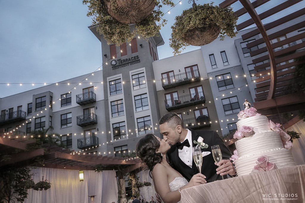 wedding reception bride and groom kiss next to wedding cake on the noor terrace pasadena